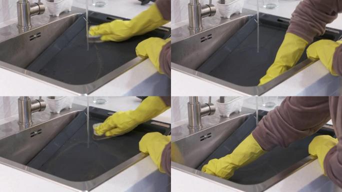 女人戴着橡胶手套在自来水下清洁厨房水槽中的烤箱烤盘。