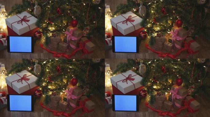 枞树下的圣诞红色工艺礼品盒和平板蓝色模型屏幕