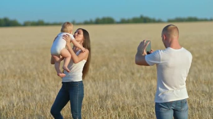 当一个美丽的女人围着一个婴儿时，年轻人在手机上拍摄了一段视频。在麦田里拍照，一位博主制作了一段视频。