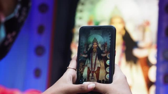 一名印度女孩使用手机在puja pandal上用智能手机点击Durga Maa idol的照片
