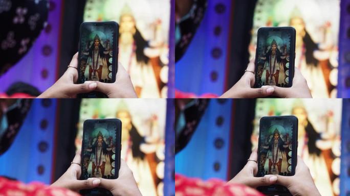 一名印度女孩使用手机在puja pandal上用智能手机点击Durga Maa idol的照片