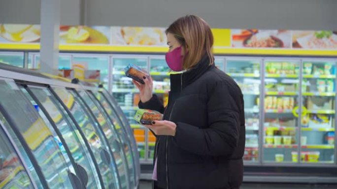 一位戴着口罩保护Covid-19的妇女站在冷藏库的货架前。有选择性的重点