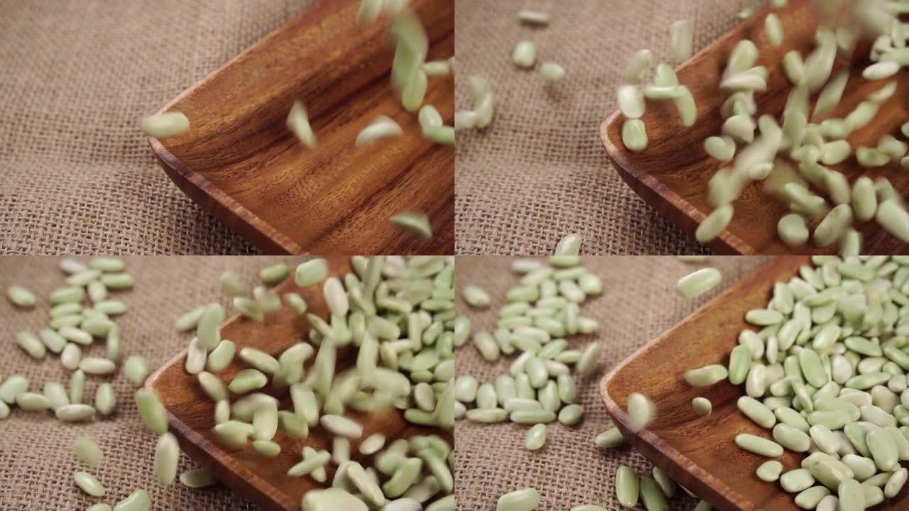 未煮熟的绿色Verdina豆掉入乡村粗糙粗麻布上的木碗中