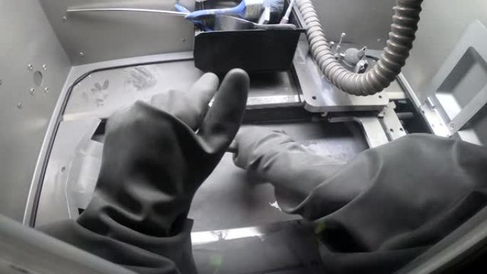 穿着孤立的黑色橡胶手套的工人清洁3d金属打印机内部的刷子打印平台。戴手套的人清洁工业机器内的金属粉末