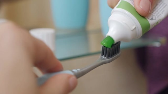 妇女在浴室的手将绿色牙膏从管子上挤到牙刷上清洁牙齿，早晚程序，卫生。慢动作