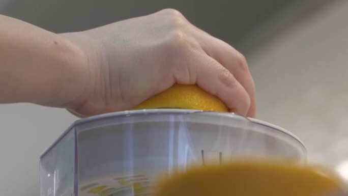 用榨汁机挤橙子的人手特写。健康饮料概念。