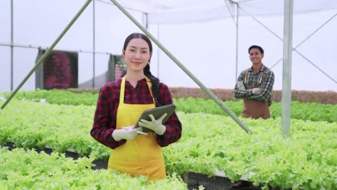 亚洲男女农民检查温室水培农场种植绿色新鲜蔬菜的质量水培系统农场检查有机蔬菜产品的质量