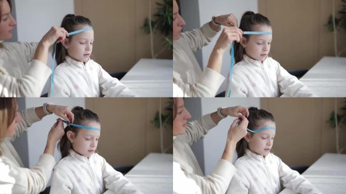 母亲测量了女儿的头围和手臂长度。白人小女孩在家