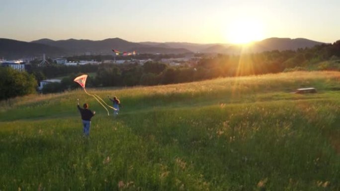 4k母女在山上奔跑，风筝飞扬，背景为日落
