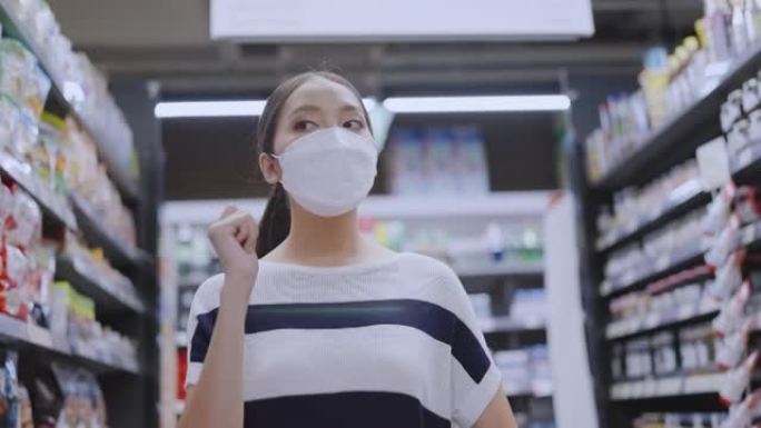 亚洲女性家庭主妇拉着手推车在商场超市挑选商品，女性戴着口罩在商场商店里行走寻找消费品