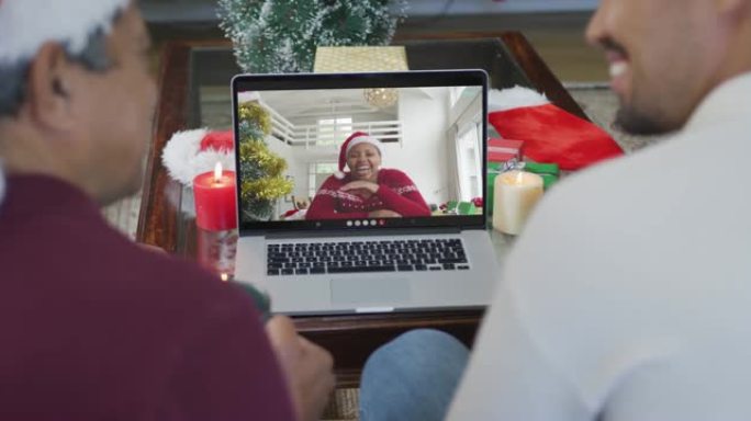 带有圣诞老人帽子的混血儿父子使用笔记本电脑进行圣诞节视频通话，屏幕上有女人