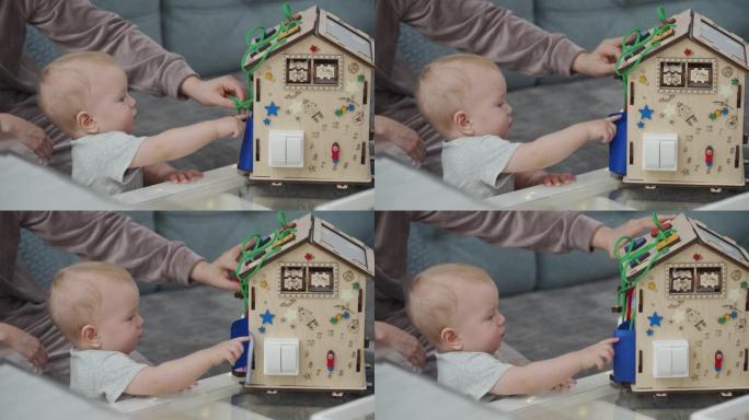 母亲和她的男婴在家里玩木制繁忙的蒙特梭利教育玩具。儿童忙板。