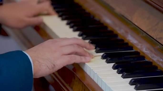一个穿着蓝色衬衫的男人的手按一架旧钢琴唱歌。