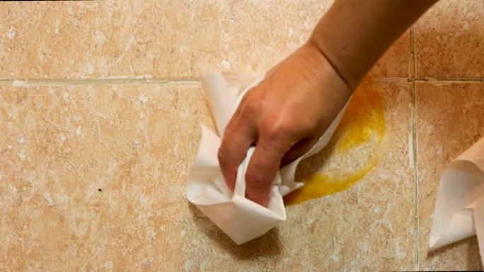 一个破碎的鸡蛋的俯视图，拍打在厨房的地板上，可以看到蛋黄，外壳和白色，一个女孩用厨房纸清洁地板
