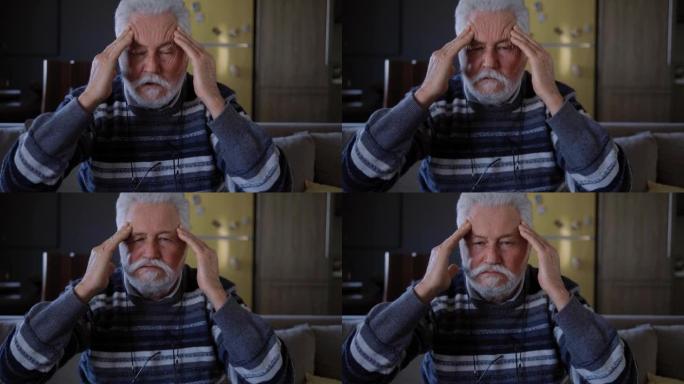 老人按摩头部，看着相机。头痛和头部健康问题。患有偏头痛的老人
