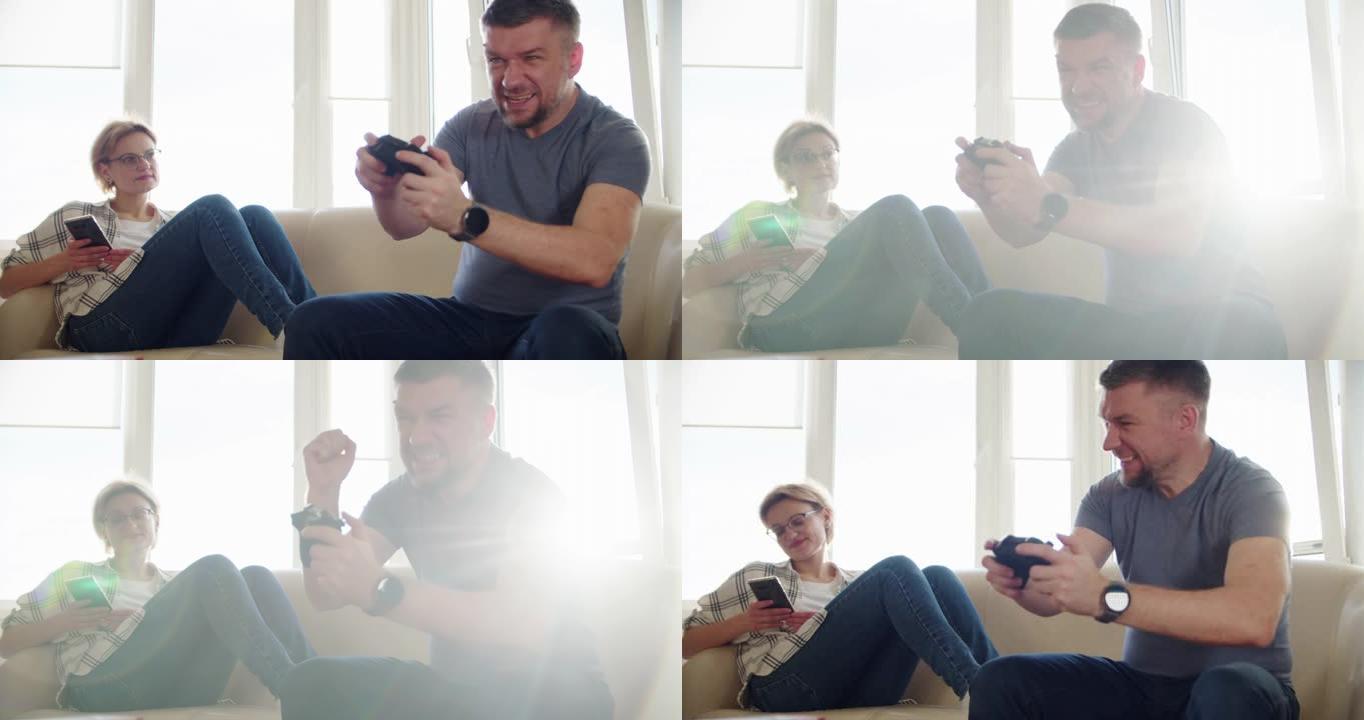 慢动作。幸福的夫妻坐在沙发上玩电子游戏，在恋爱中使用控制器一起玩在线电子游戏。