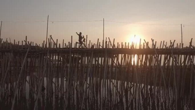 空中平移拍摄了一个小孩在日落时在河上的竹桥上奔跑的镜头