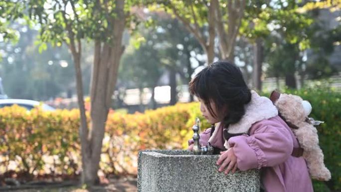 女孩在操场上的垂直水龙头里喝水