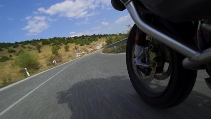 摩托车骑在自然界的道路上。在颠簸的沥青路面上关闭车轮。以100 fps记录。