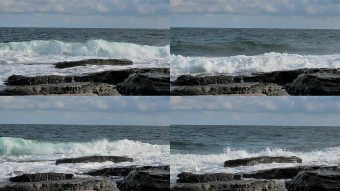 海浪溅落在蓝色海洋背景的岩石海岸上。波涛汹涌的岩石海岸线在暴风雨中席卷而来。海浪用泡沫在石头上破裂。