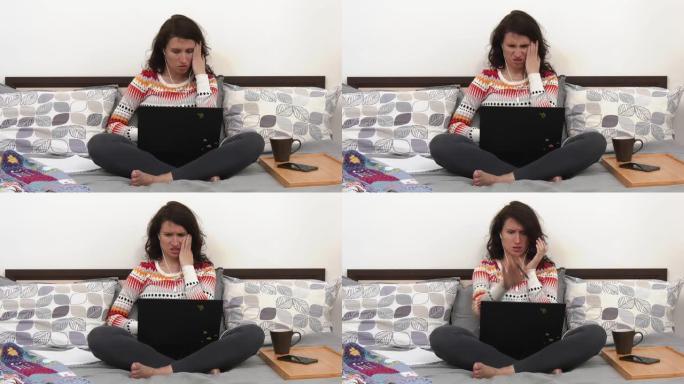 一名妇女坐在她的床上，使用她的笔记本电脑，在屏幕上看到一个可怕的场景，并做出情绪反应