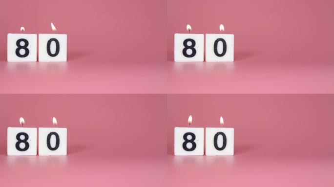 一根方形蜡烛，上面写着80号在庆祝生日或周年纪念日的粉红色背景上被点燃和吹灭
