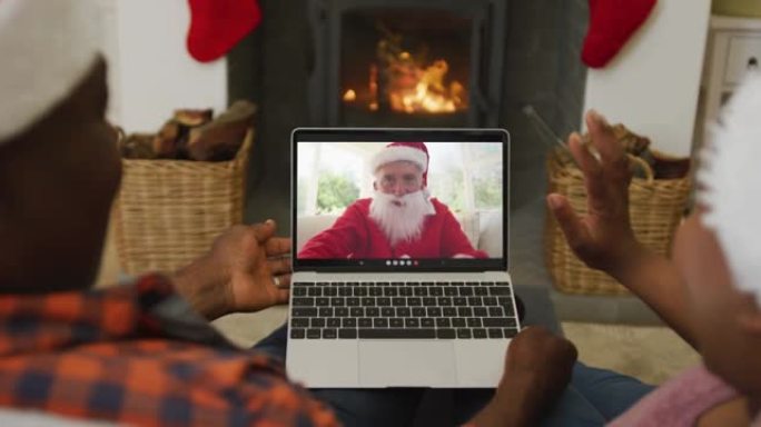 非洲裔美国夫妇戴着圣诞老人帽子，使用笔记本电脑进行圣诞视频通话，屏幕上有圣诞老人