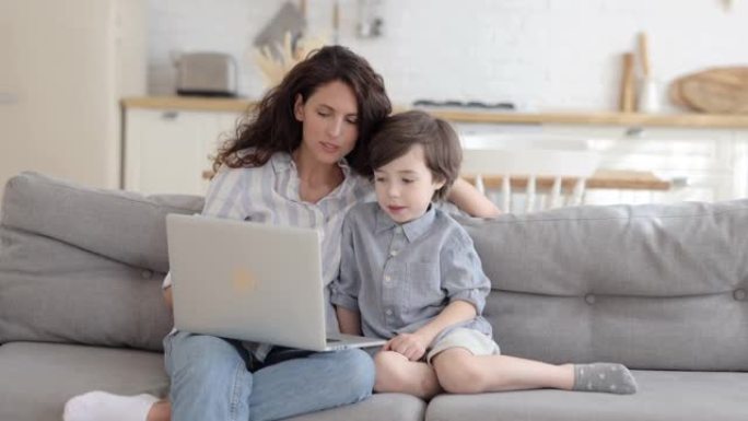 年轻的妈妈和学龄前男孩用笔记本电脑娱乐或教育在家观看学习视频