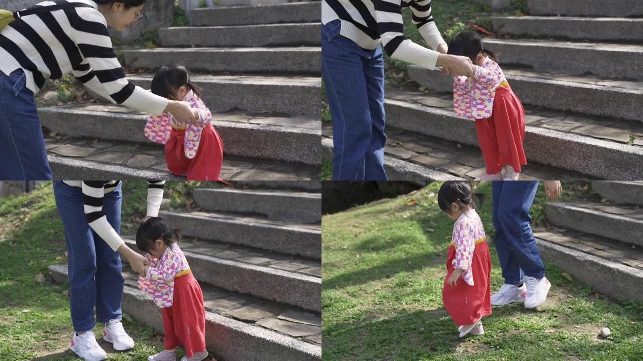 穿着日本传统服饰的可爱亚洲幼童，在妈妈的帮助下，从石阶下到草坪上，在公园里玩耍。