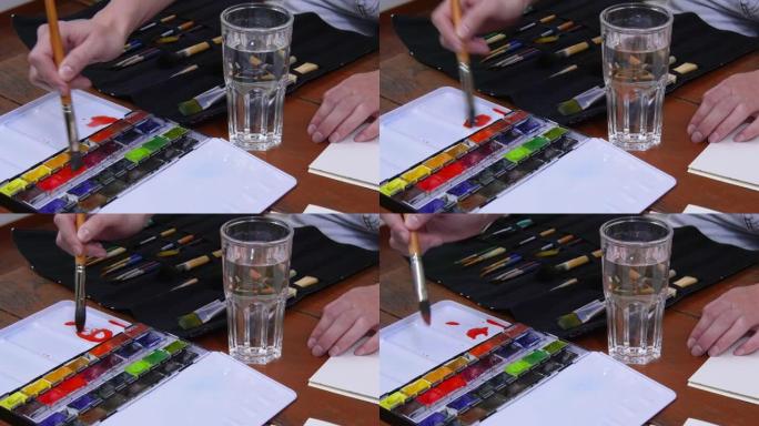 艺术家用红色水彩颜料和一杯水蘸艺术画笔