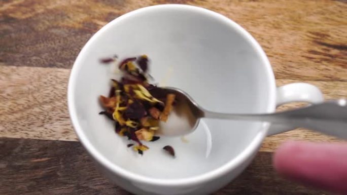 一茶匙将干草本水果花茶放在木桌上的白杯中