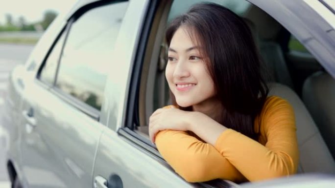 年轻漂亮的亚洲女性得到新车。她看着窗外非常高兴和兴奋。灿烂的日子里，微笑的女性驾驶车辆在路上