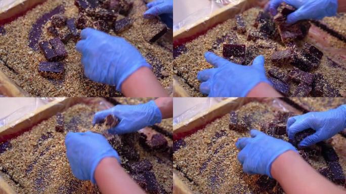 戴着蓝色手套的手覆盖着坚果中的小果酱。紫色果冻条与切碎的核桃混合在一起。侧面特写。
