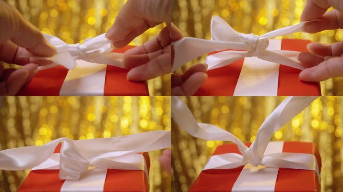双手从礼品盒中拉出白色丝带，带有金色闪光背景，圣诞节和假期概念。