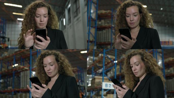 年轻的女商人站在工厂储藏室里使用手机