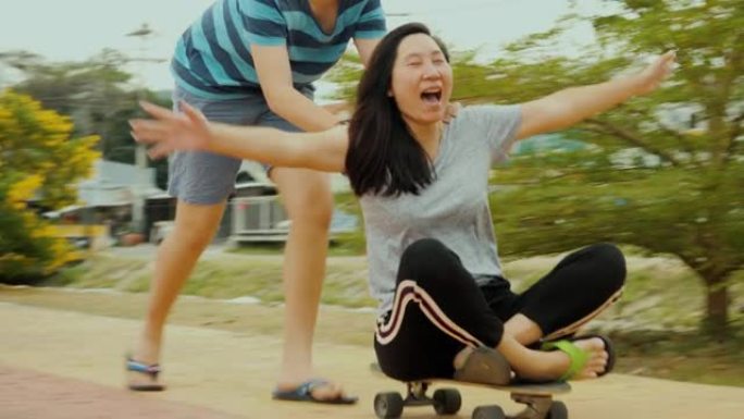 快乐的亚洲男孩推动他坐在滑板上的母亲一起享受户外生活方式的理念。