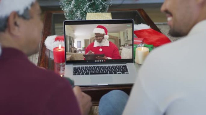 带有圣诞老人帽子的混血儿父子使用笔记本电脑进行圣诞视频通话屏幕上的圣诞老人