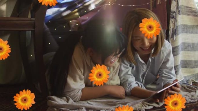 橙色花朵的动画在快乐的亚洲母女在家中使用平板电脑
