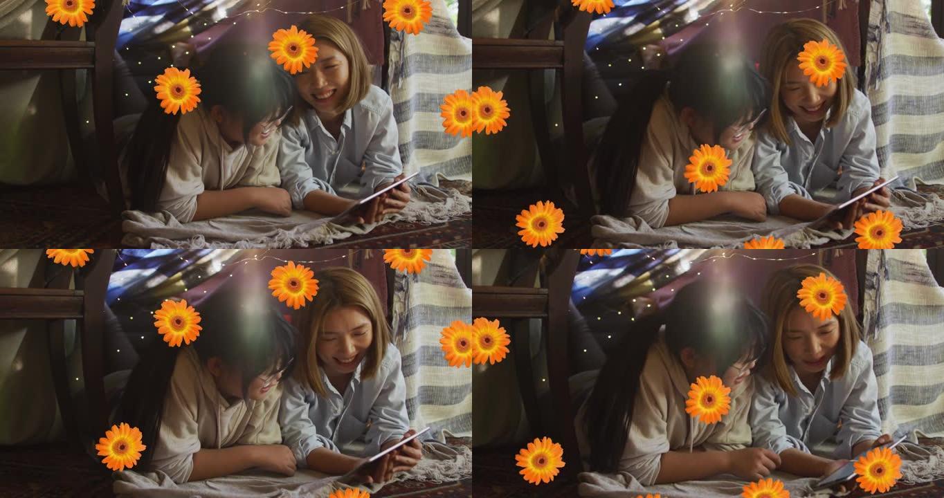 橙色花朵的动画在快乐的亚洲母女在家中使用平板电脑