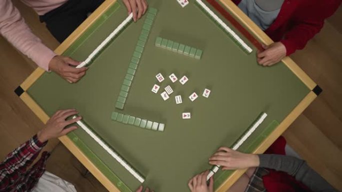 春节期间，在家里一起玩瓷砖游戏时，从人们的双手上方观看并在桌子上放下绿色的麻将碎片