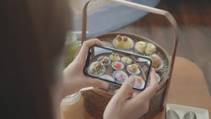 东南亚妇女在分享到社交媒体之前使用移动相机捕获泰国甜点