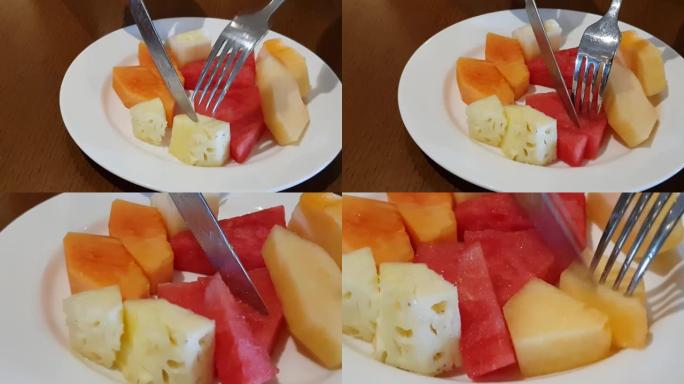 吃新鲜多汁的水果沙拉，木瓜，甜瓜，菠萝和西瓜配白盘健康早餐