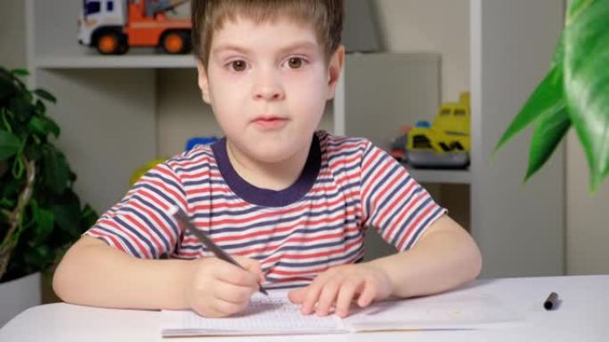 一个学龄前男孩写咒语，微笑并逃离桌子