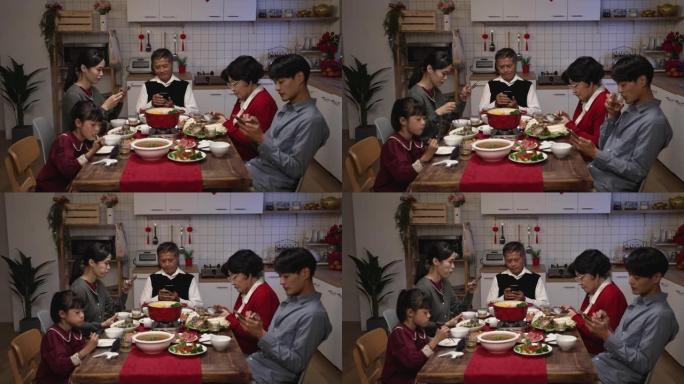 亚洲家庭，混血儿在家里除夕夜在餐桌上吃团圆饭时玩手机，无视对方