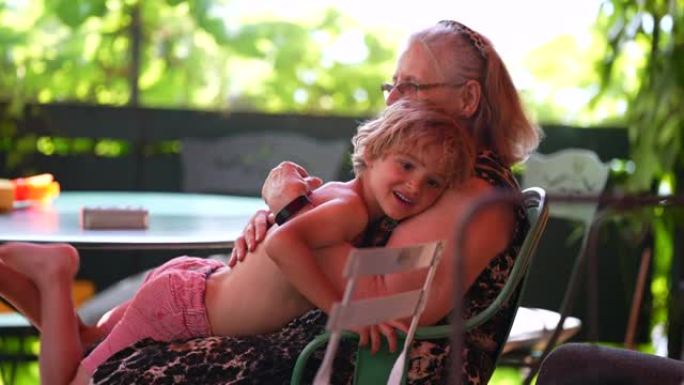 孙子在家里阳台上与祖母依偎在一起，现实生活中的家庭拥抱亲情