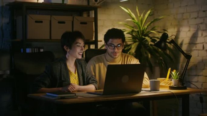 美丽的年轻夫妇坐在一台打开的笔记本电脑前谈笑风生