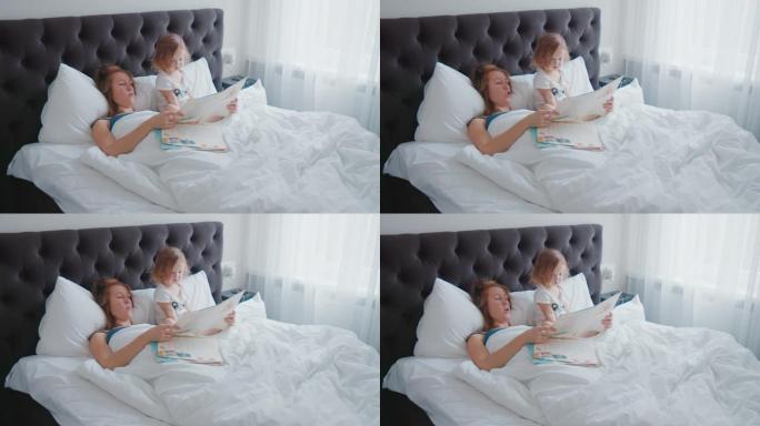 晨床阅读。年轻女子在明亮的现代卧室的床上为她蹒跚学步的孩子读这本书