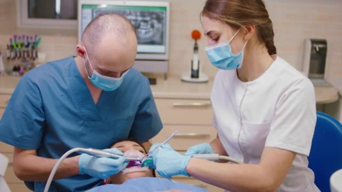 女患者在牙科诊所探望牙医，他的助手女士戴着防护口罩治疗患者的龋齿
