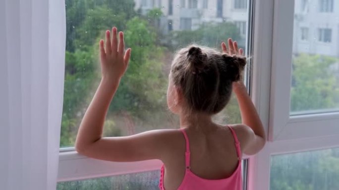 女孩站在窗前，看着雨。孩子在窗前悲伤。