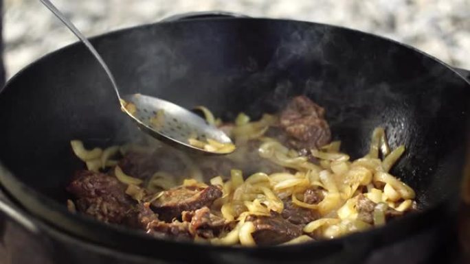 用开槽的勺子在大锅中搅拌肉和洋葱